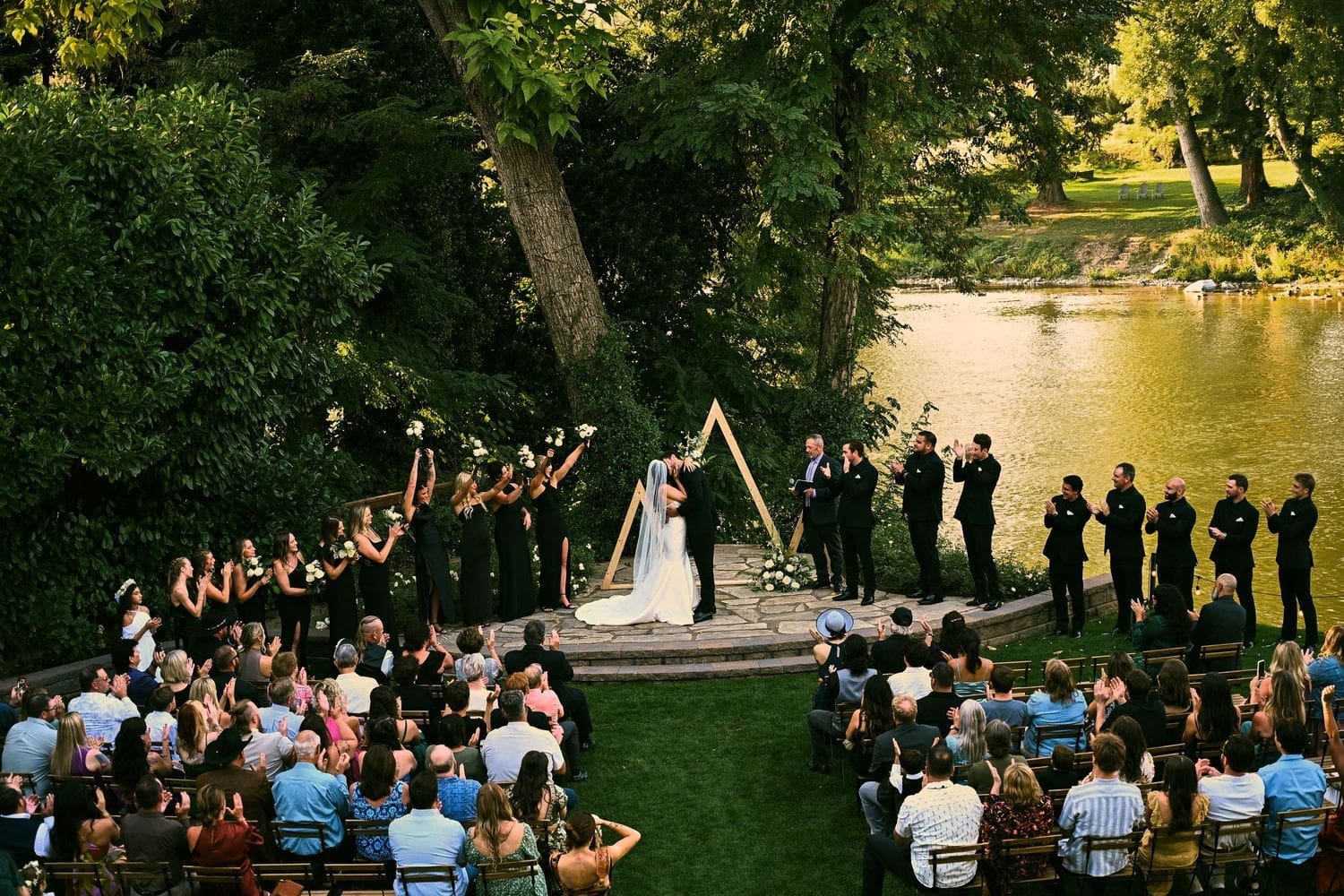 Outdoor wedding ceremony in a lush garden setting with guests seated in white chairs at sunset at A River House in Grants Pass, Oregon