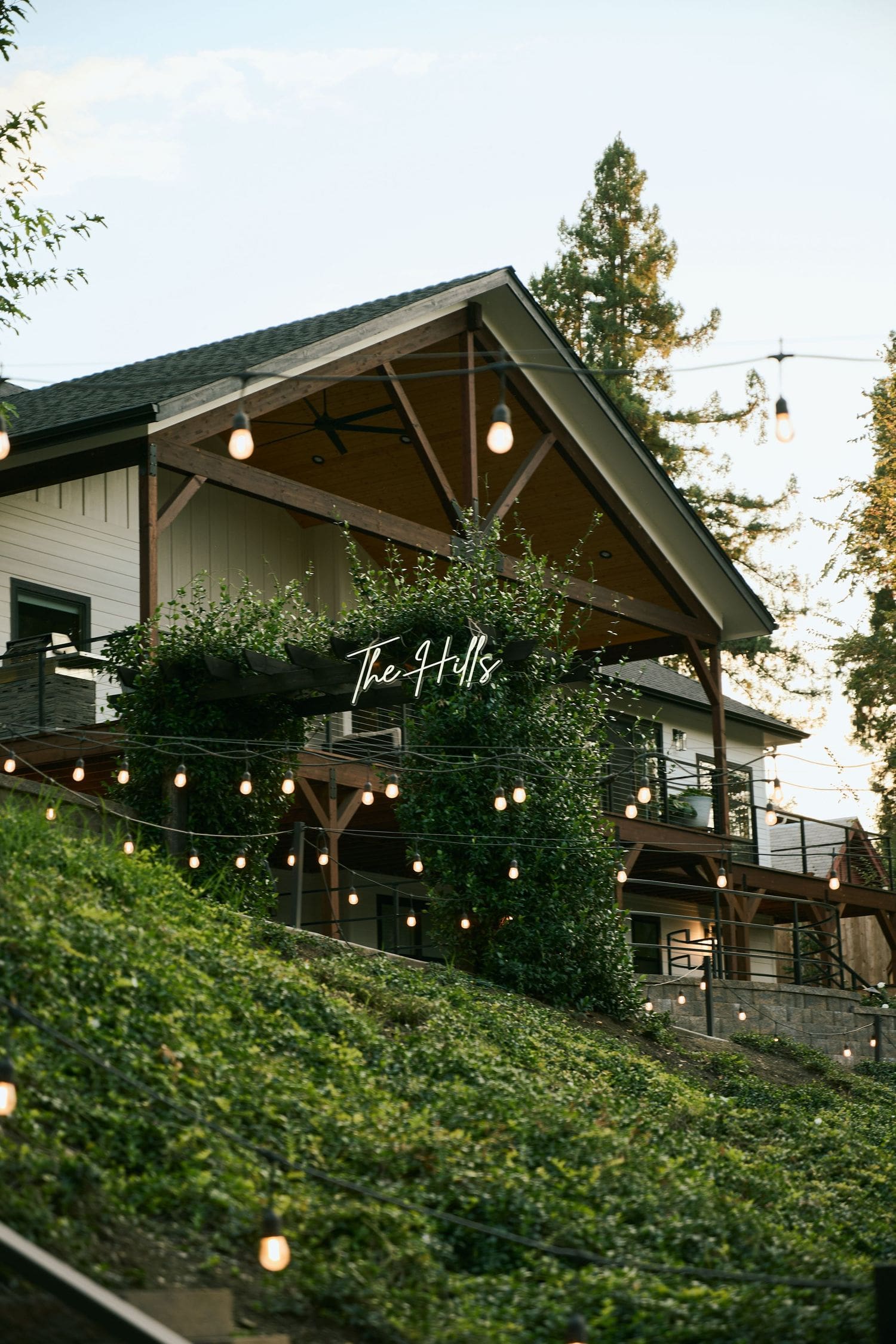 Rustic hillside restaurant with string lights and a neon sign glowing at dusk near A River House wedding venue