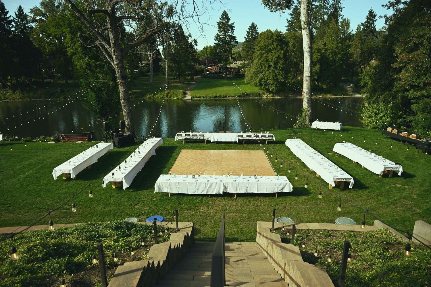 Outdoor wedding reception with long white tables on a green lawn beside a pond in Southern Oregon