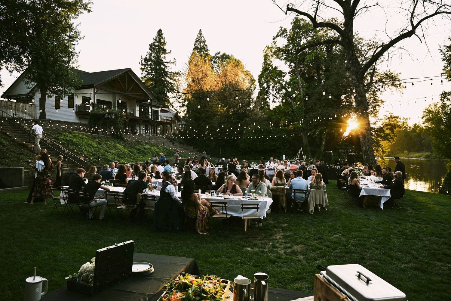 Outdoor wedding reception at sunset with guests dining under string lights at A River House in Grants Pass