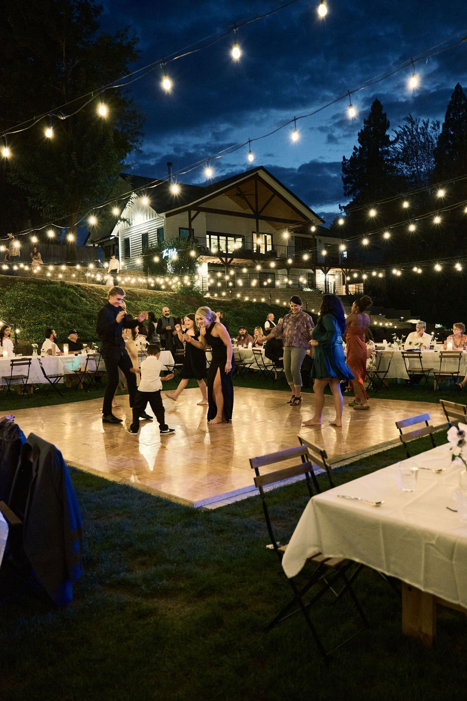Evening wedding reception with guests dancing on a wooden dance floor under string lights in Southern Oregon