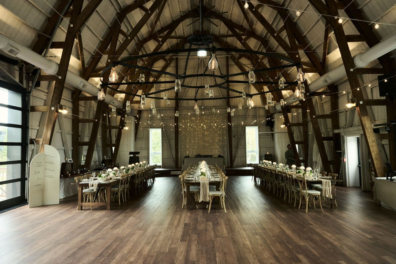 Rustic barn wedding reception with long tables, string lights, and wooden beam ceilings at Crescent Hill Acres