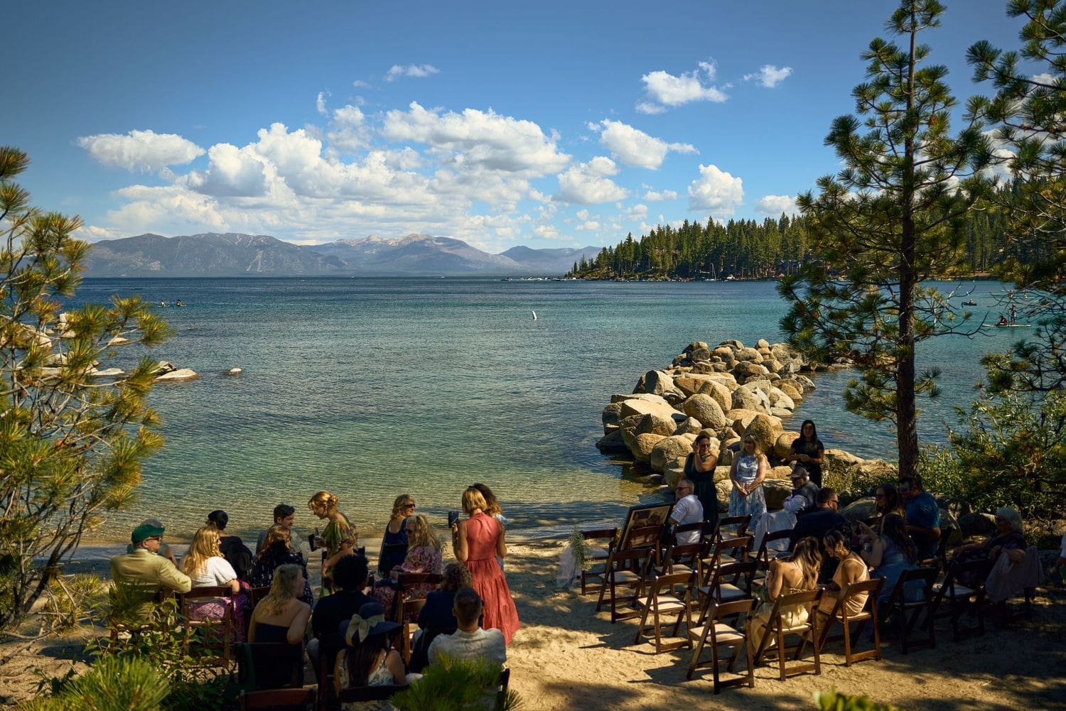 Outdoor wedding ceremony by the Lake Tahoe shore with guests seated among pine trees and mountains