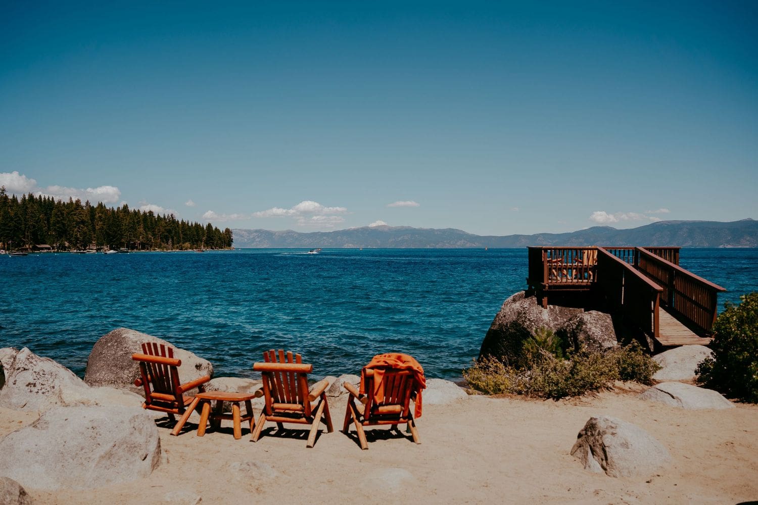 Wooden Adirondack chairs on a sandy Lake Tahoe shore with turquoise water and mountains under a blue sky
