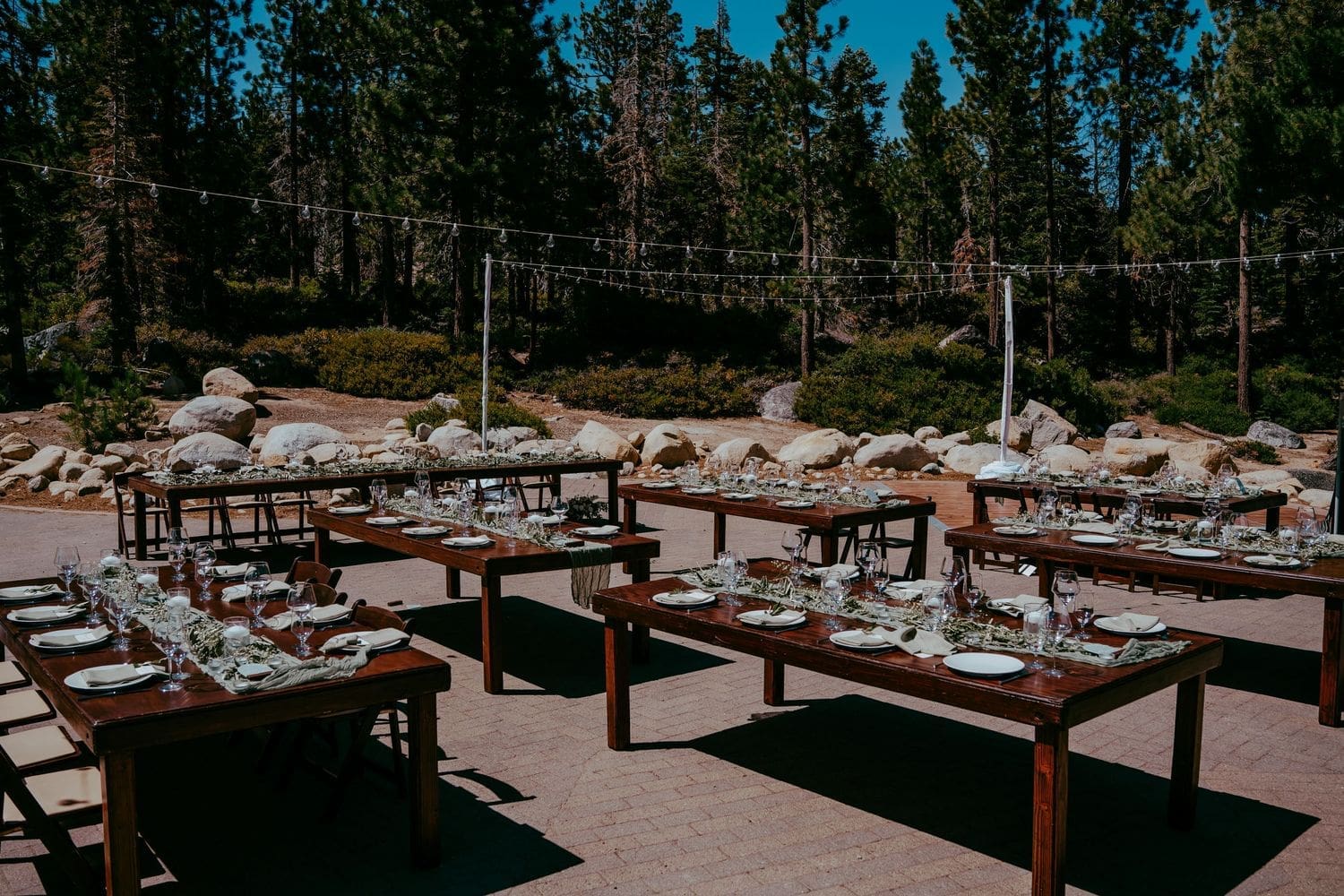 Outdoor rustic wedding reception with wooden farm tables surrounded by pine trees and string lights at Lake Tahoe