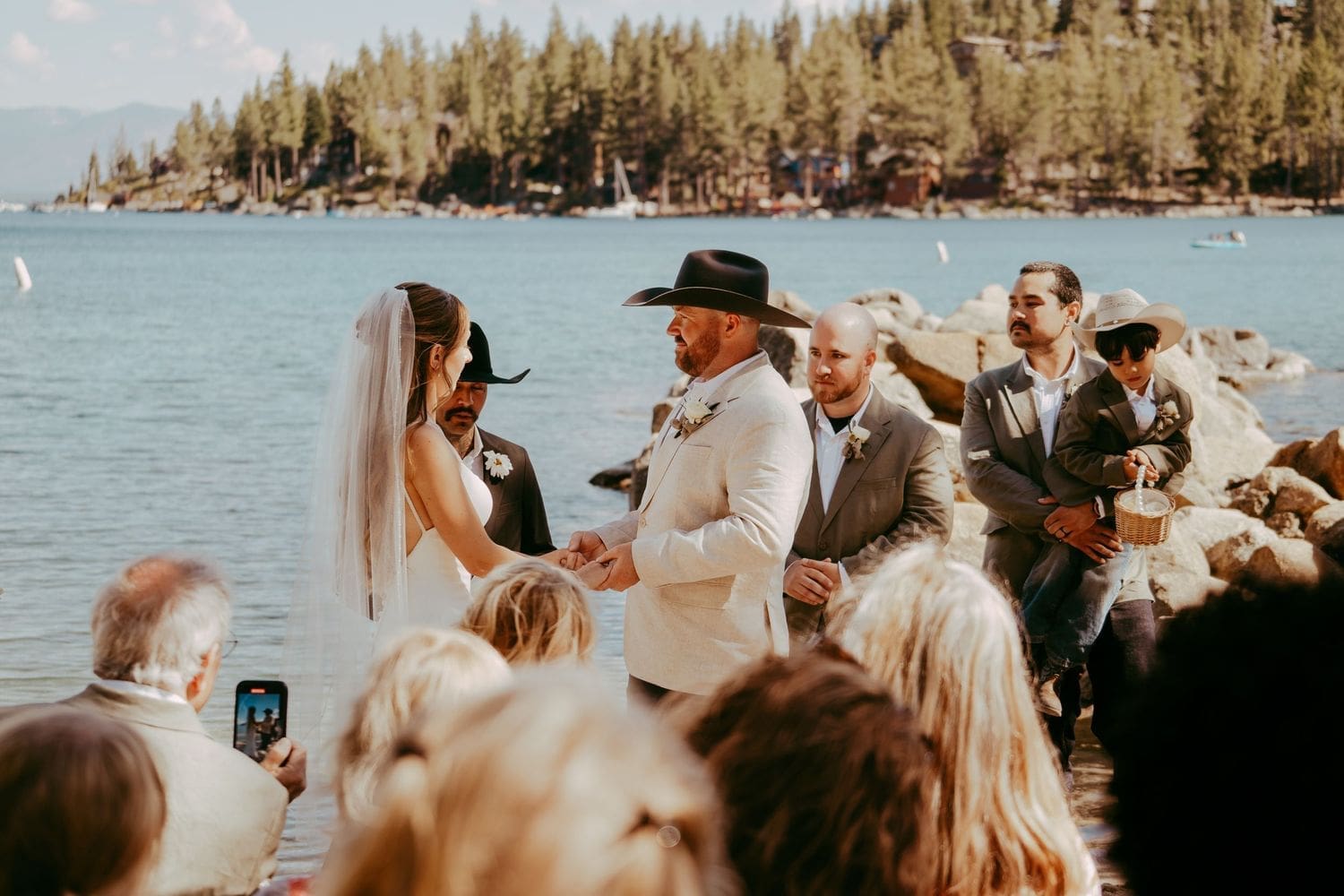 Outdoor lakeside wedding ceremony with the bride and groom exchanging vows among pine trees at Lake Tahoe