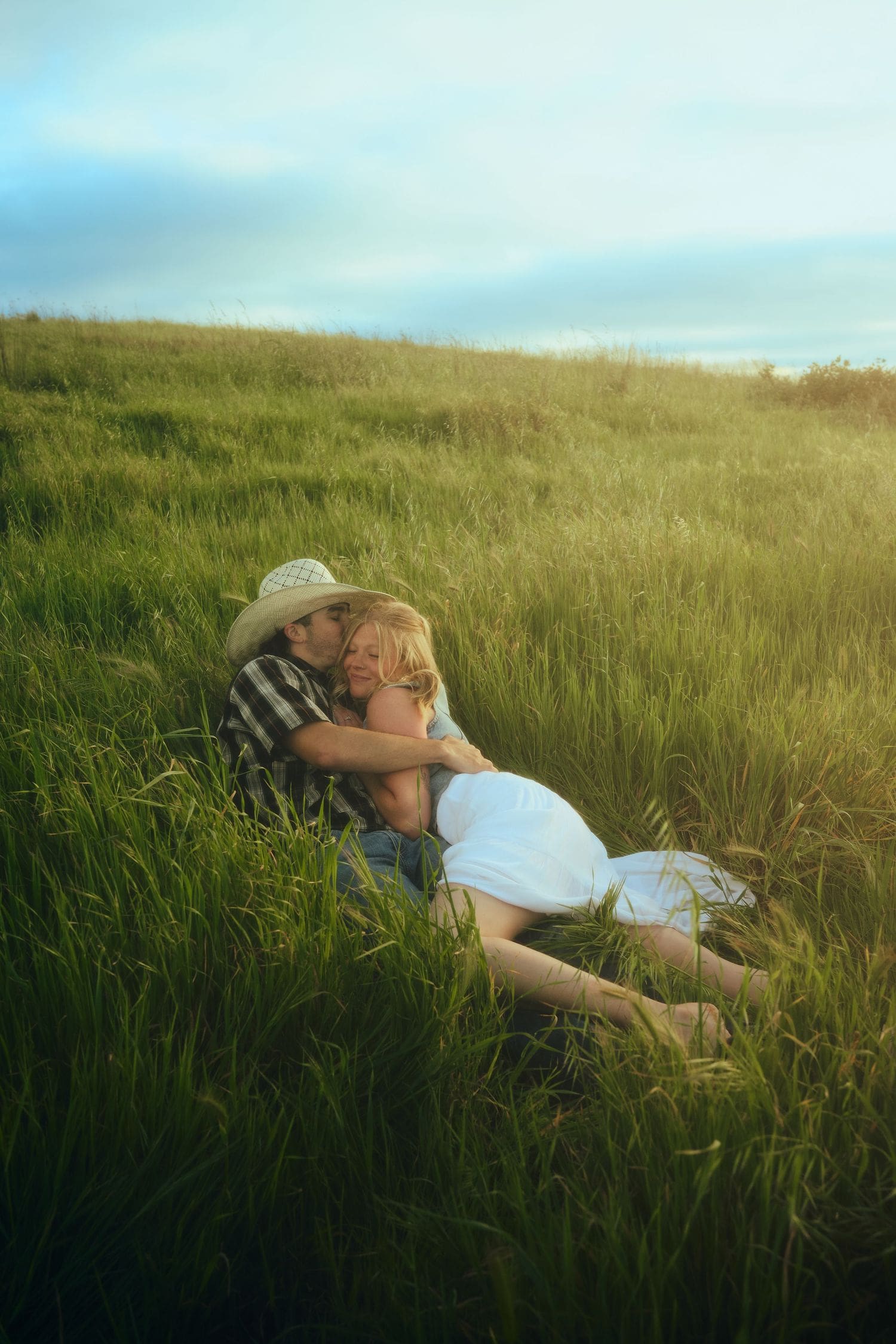 Romantic couple embracing in a lush green field at golden hour during their engagement session