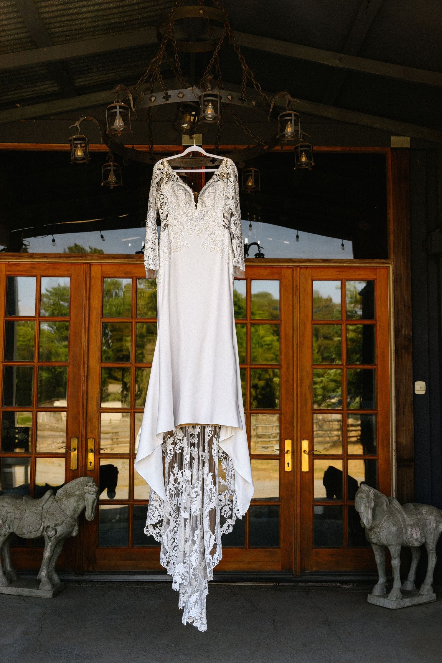 Elegant lace wedding dress with long sleeves hanging from a chandelier at Sovignon Ranch wedding venue