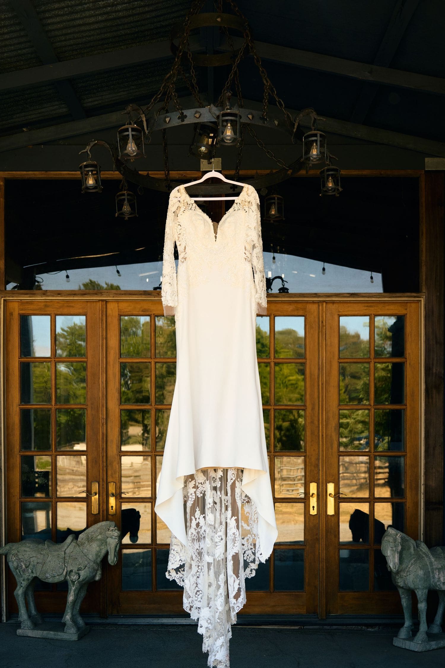 Lace wedding dress hanging from a rustic chandelier above French doors at Sovignon Ranch